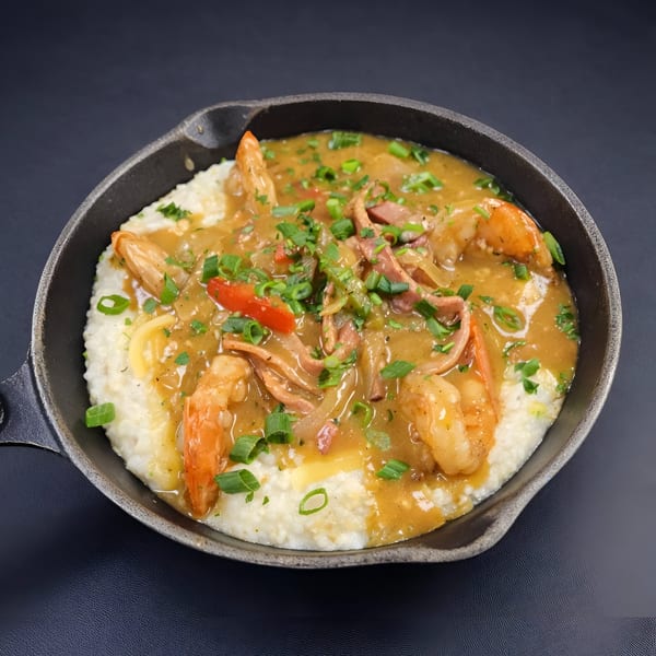 Shrimp and grits with gravy, sausage, peppers, and green onions in a cast iron skillet.