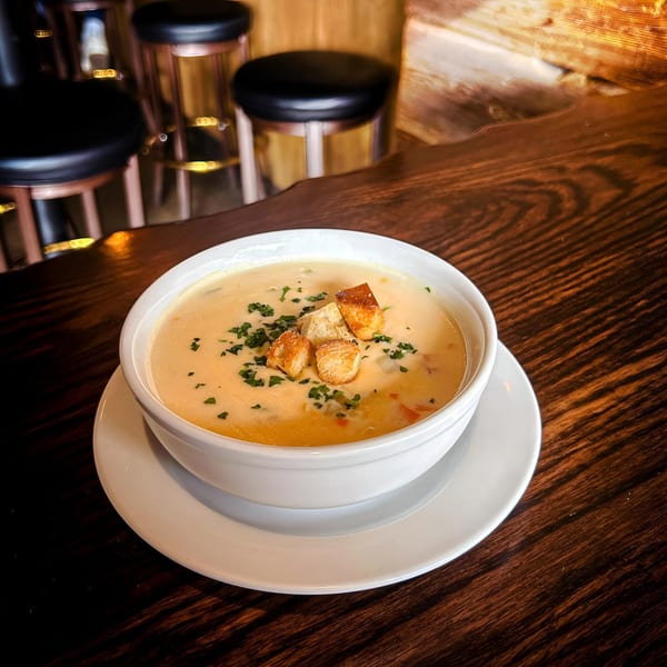 Creamy soup with croutons and herbs in a white bowl on a dark wooden table with bar stools.
