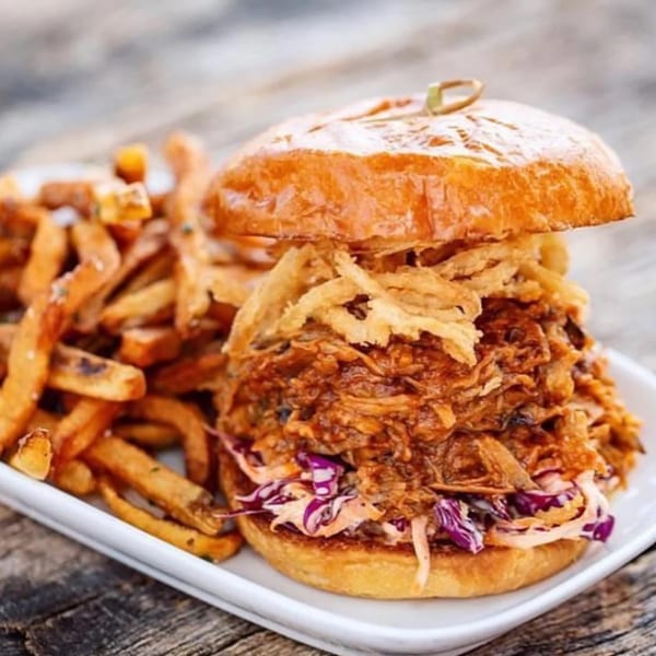 Pulled pork sandwich with coleslaw and crispy onions, served with a side of sweet potato fries.