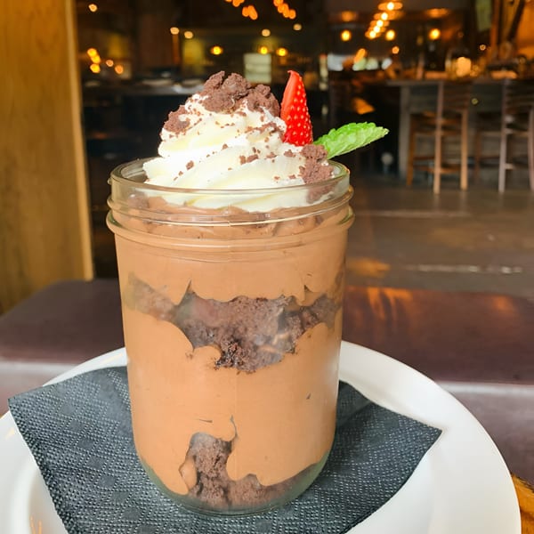 Chocolate dessert in a mason jar, topped with whipped cream, cookie crumbles, strawberry, and mint.
