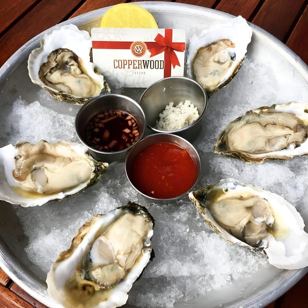 Six fresh oysters on a bed of ice with cocktail sauce, mignonette, and a Copperwood Tavern gift card.