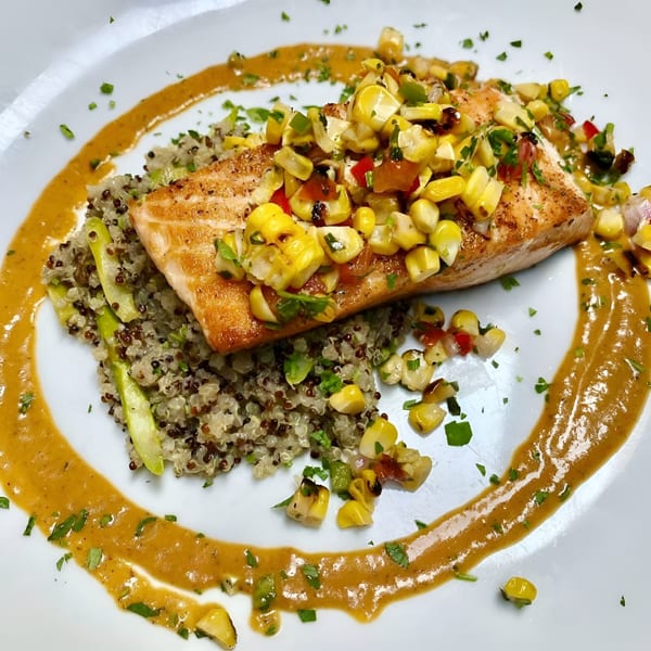 Pan-seared salmon with corn salsa, quinoa, asparagus, and a savory sauce on a white plate.