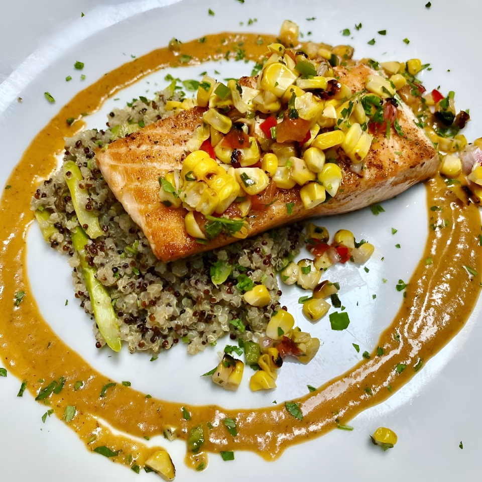 Pan-seared salmon with corn salsa, quinoa, asparagus, and a savory sauce on a white plate.
