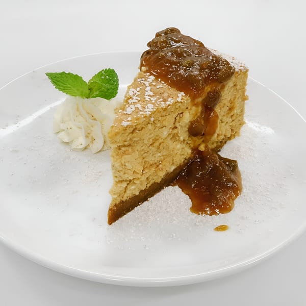 A slice of cheesecake topped with apple compote, powdered sugar, whipped cream, and mint.