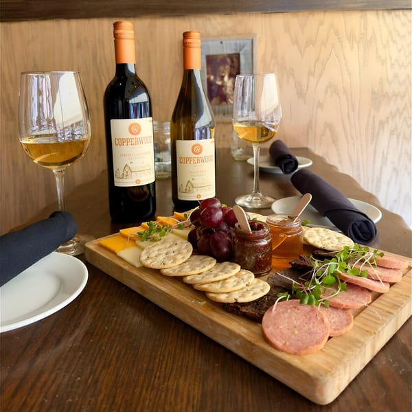 A charcuterie board with cheeses, crackers, grapes, meats, and two bottles of Copperwood wine.
