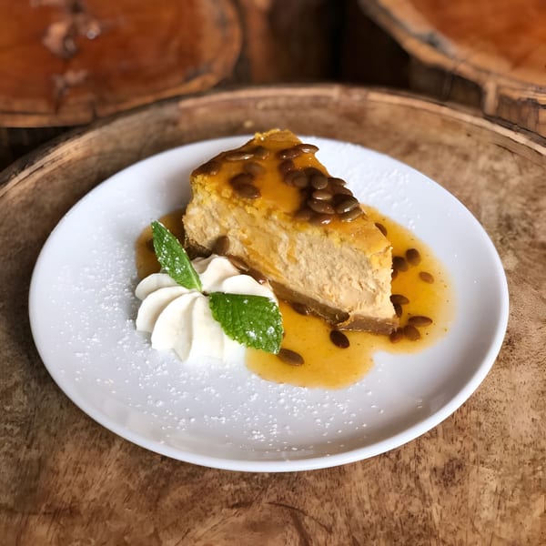 Slice of pumpkin cheesecake with passionfruit sauce, whipped cream, and mint on a white plate.
