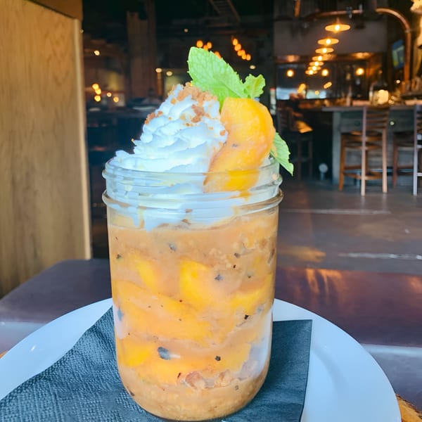 A mango dessert in a mason jar with whipped cream, mint, and cookie crumbles.