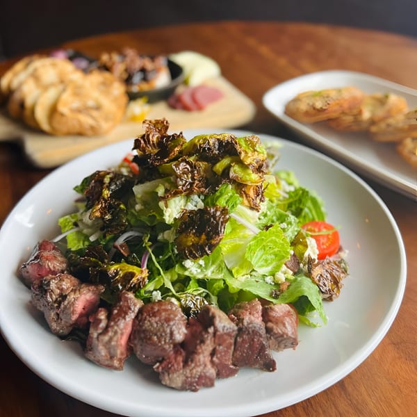 Steak salad with roasted Brussels sprouts, lettuce, tomatoes, and feta cheese on a white plate.