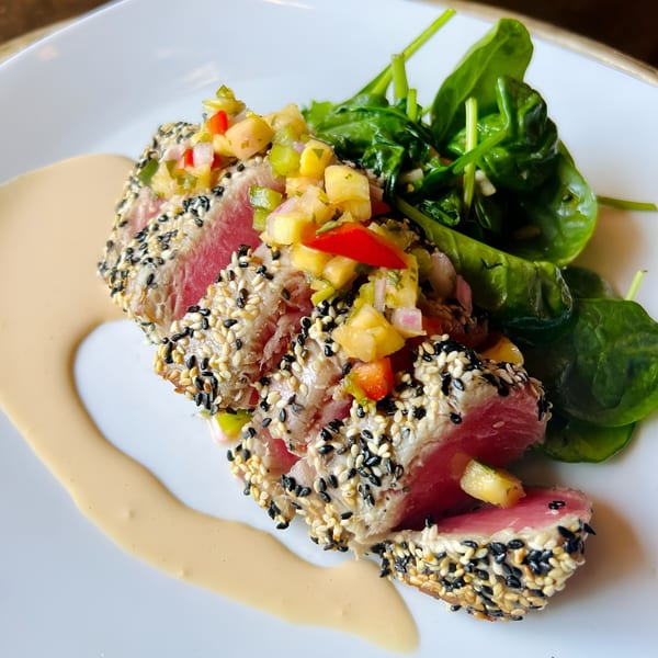 Sesame-crusted tuna with pineapple salsa and a side of fresh spinach on a white plate.